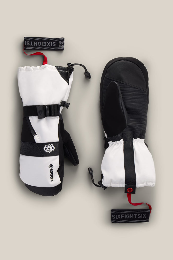 A pair of 686 Men’s GORE-TEX® SMARTY® 3-In-1 Gauntlet Mitts in black and white, with black palms, adjustable straps, red SIXEIGHTSiX wrist leashes, and prominent 686 and GORE-TEX logos, displayed on a beige background.