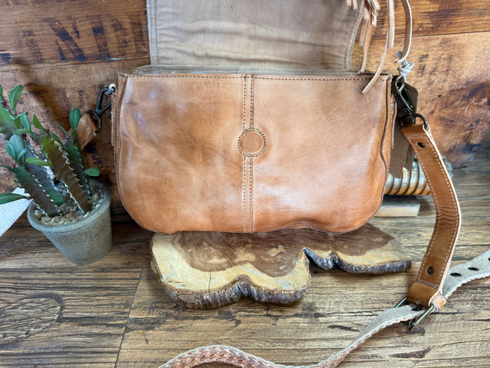 Tan suede zip-top crossbody bag with fringe accents and shoulder strap
