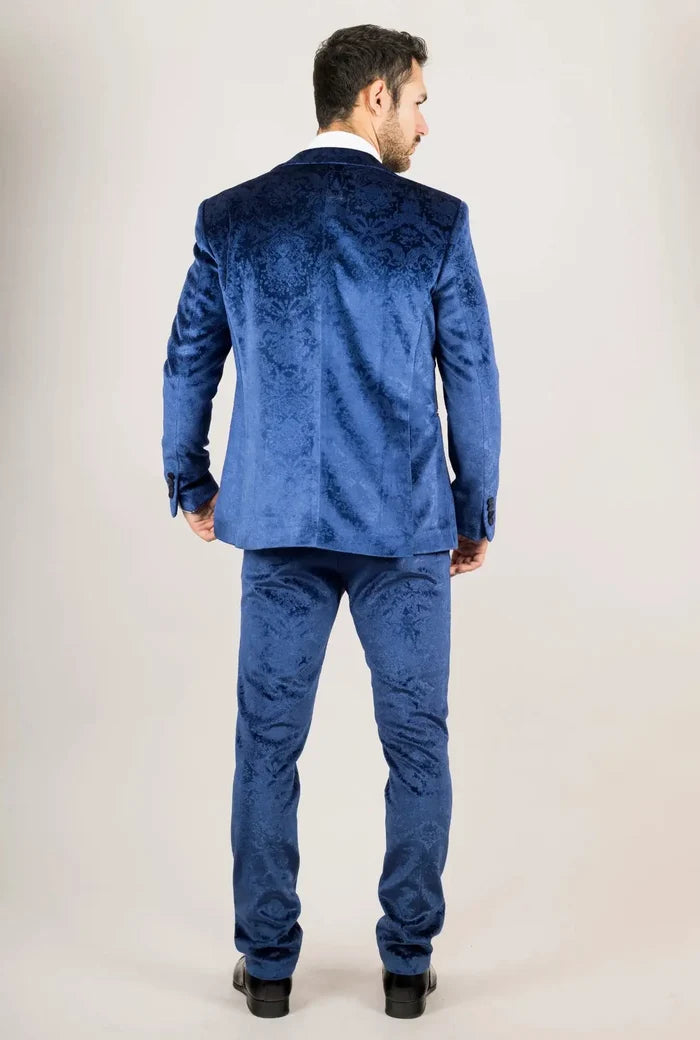 Men's blue velvet suit with intricate floral pattern, tailored fit, and matching pants, worn by a male model with dark hair and beard, standing against a plain background.
