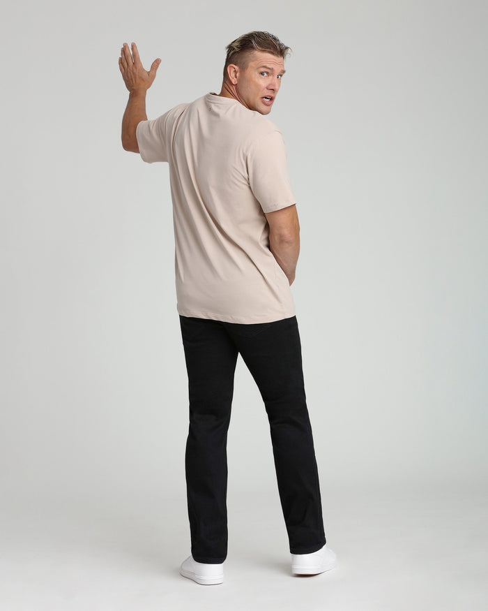 Man wearing beige short-sleeve t-shirt and black athletic fit pants with white sneakers, shown from back at three-quarter ang