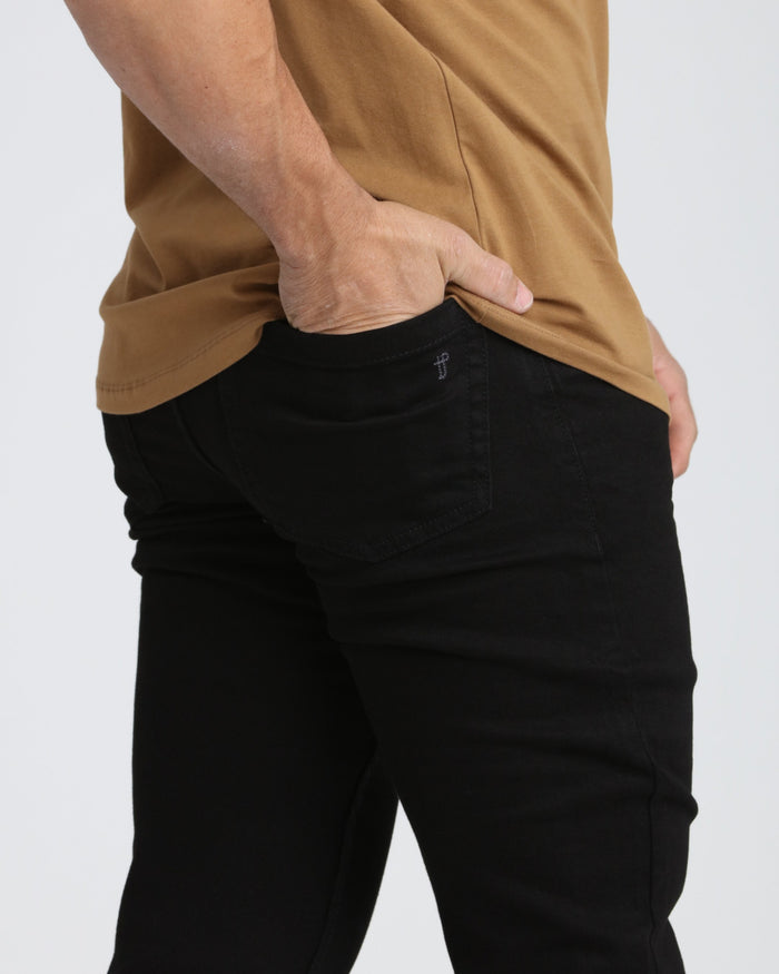 Black athletic fit jeans with visible waistband and back pocket detail on model wearing tan shirt.