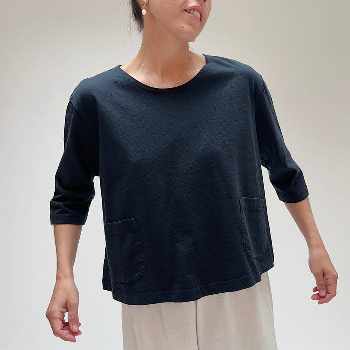 A person wearing a black, 3/4 sleeve top with two front pockets
