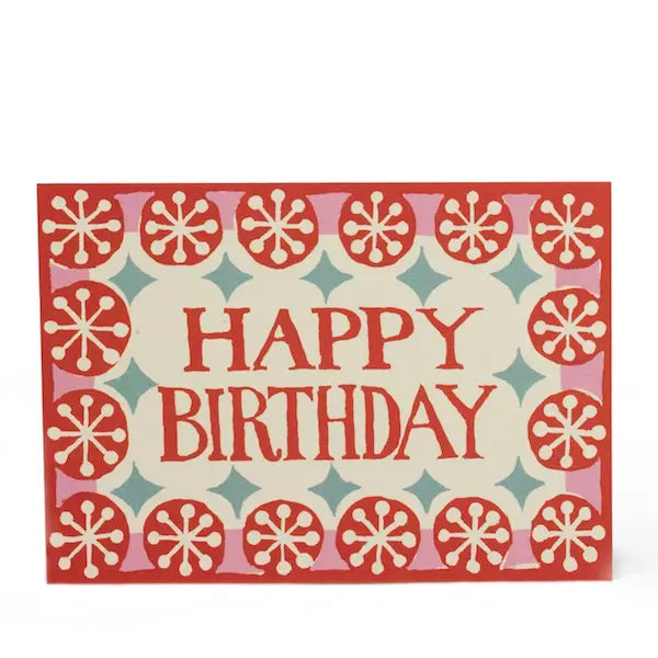 A greeting card with a coral pink background and white and red geometric patterns, with the text 'Happy Birthday' in bold letters.