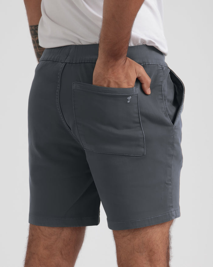 Slate-colored athletic shorts with elastic waistband and patch pockets, worn with white t-shirt.