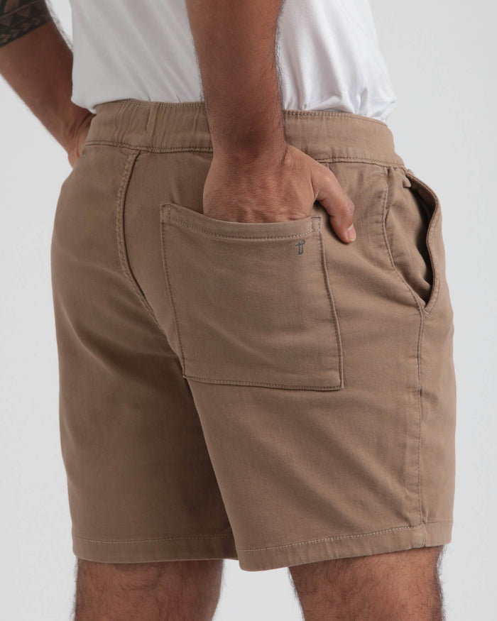 Dark khaki slim fit shorts with elastic waistband and front patch pocket, worn with white shirt.