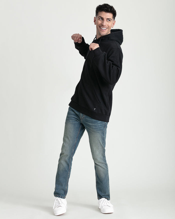 Black hoodie with drawstring hood and front pocket, worn with blue jeans and white sneakers.