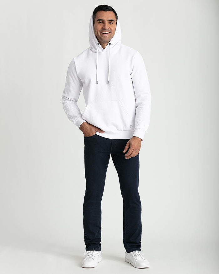 Man wearing white hoodie with drawstring hood and kangaroo pocket, paired with dark navy jeans.