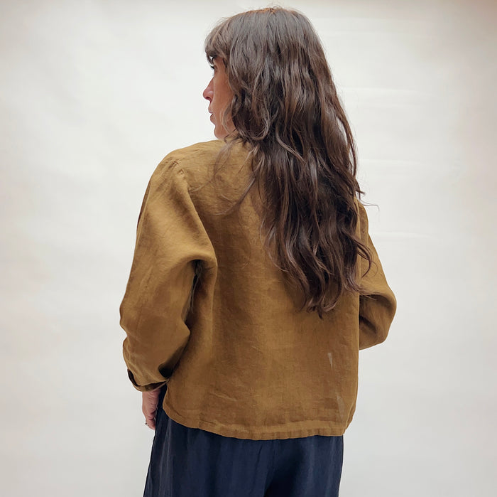 Person wearing a brown linen shirt and dark pants against a white background