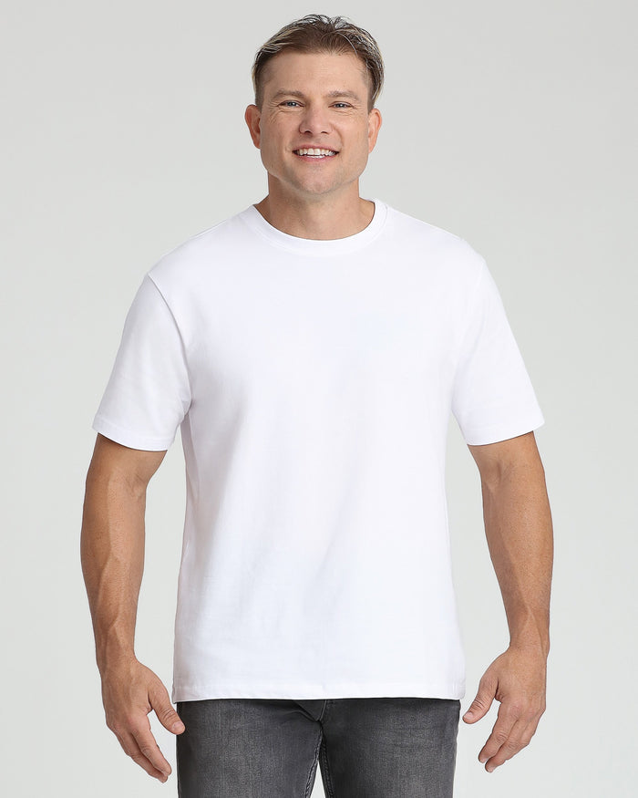 Man wearing white crew neck t-shirt with short sleeves and gray pants against neutral background.