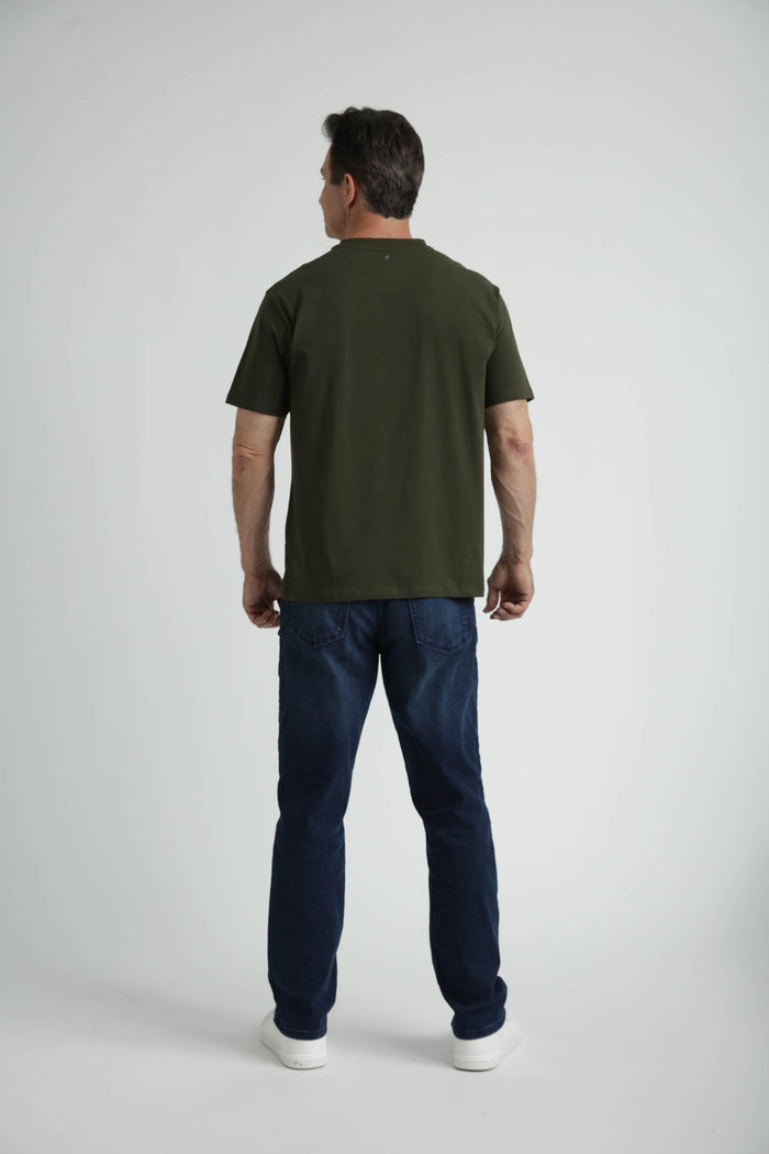 Man wearing olive crew neck t-shirt with dark jeans and white sneakers, shown from back view.
