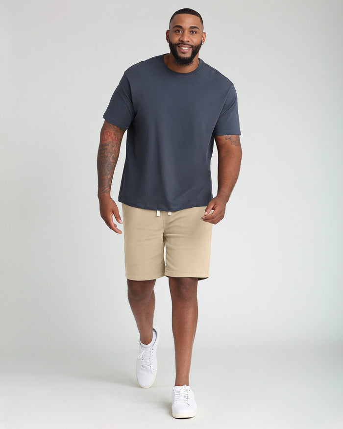 Man wearing steel blue crew neck t-shirt with beige shorts and white sneakers.