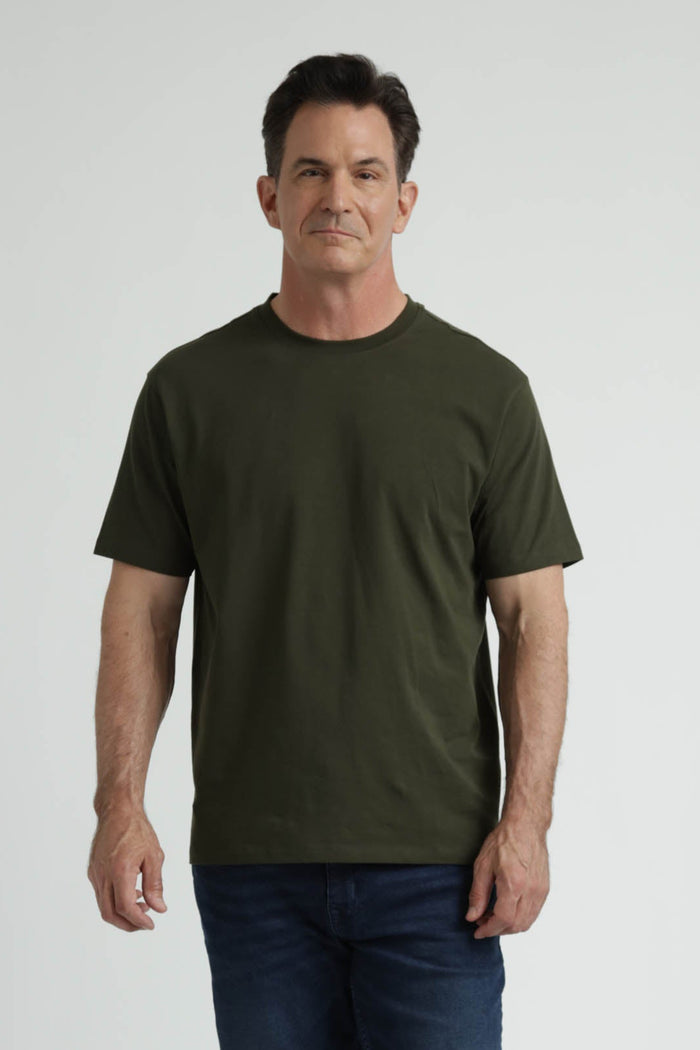 Man wearing olive green crew neck t-shirt with short sleeves and dark jeans against white background.