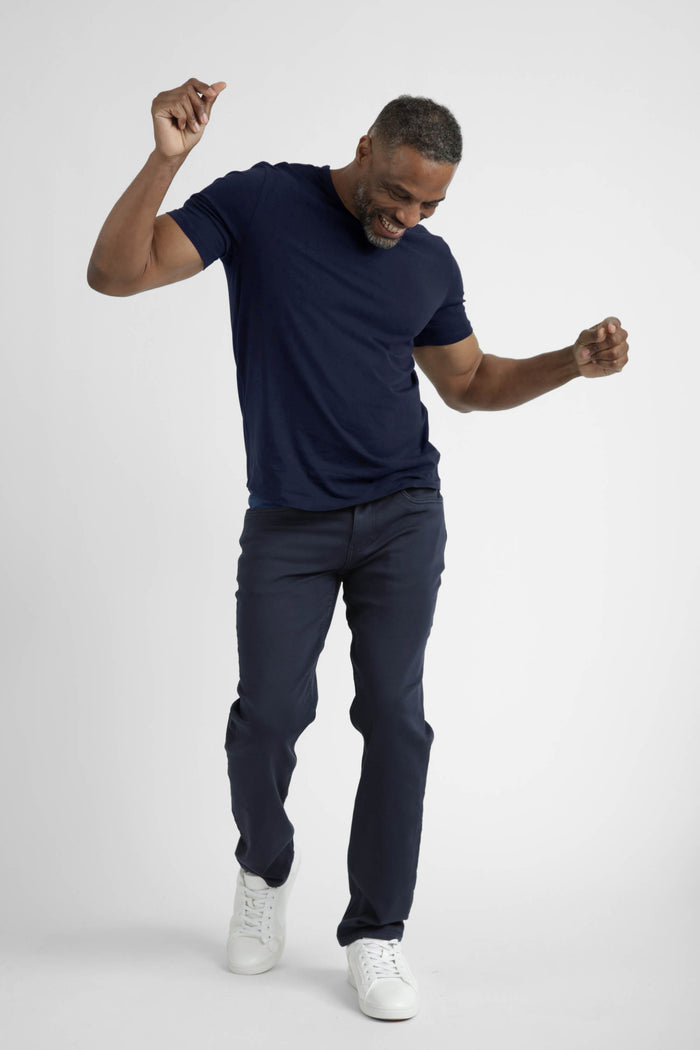 Man wearing navy crew neck t-shirt and dark pants with white sneakers, posed in a jumping motion.