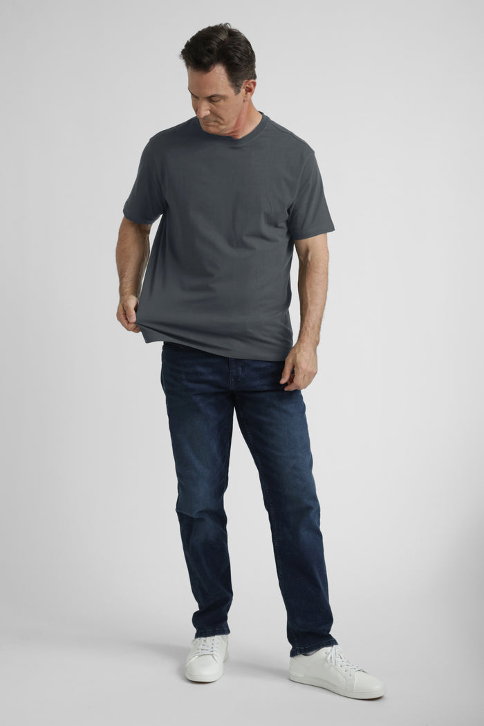 Man wearing steel gray crew neck t-shirt and dark jeans with white sneakers.