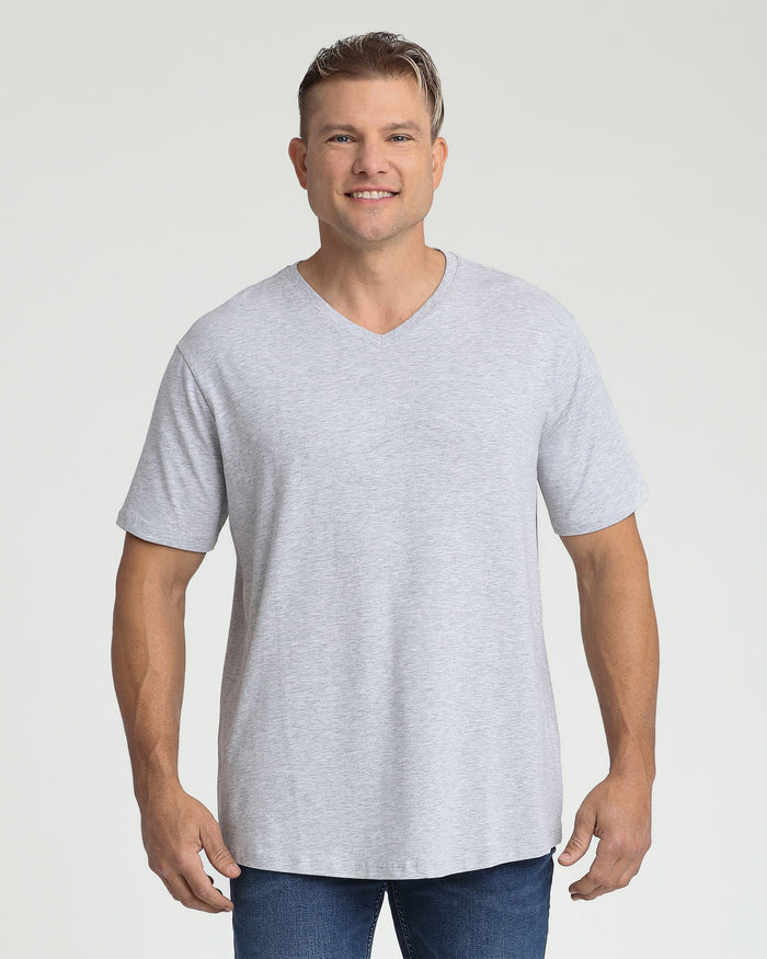 Man wearing heather grey v-neck t-shirt with short sleeves and dark jeans against white background.