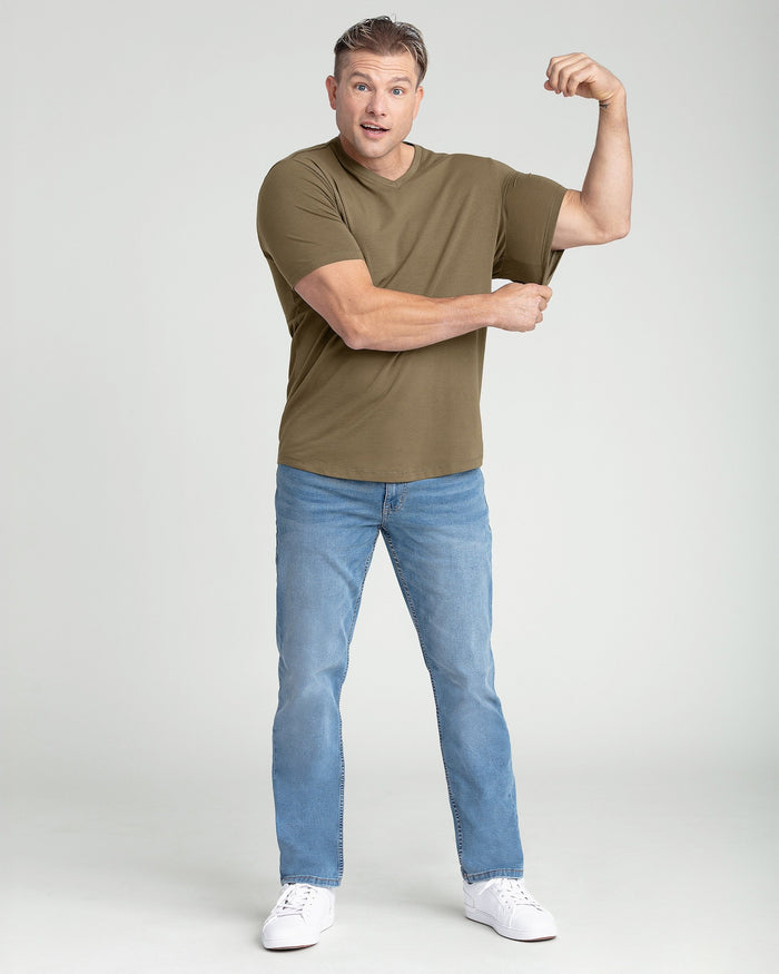 Man wearing military olive v-neck t-shirt with blue jeans and white sneakers.