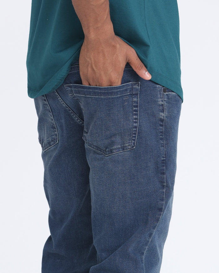 Man wearing midnight blue skinny fit jeans with hand in pocket and teal shirt visible above.