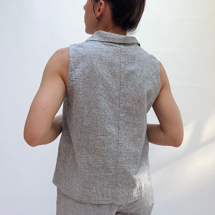 Person wearing a gray sleeveless vest and pants against a white background, viewed from the back