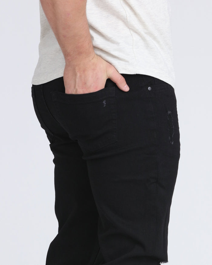 Black slim fit jeans with ripped details on the thigh, worn with a light gray top.