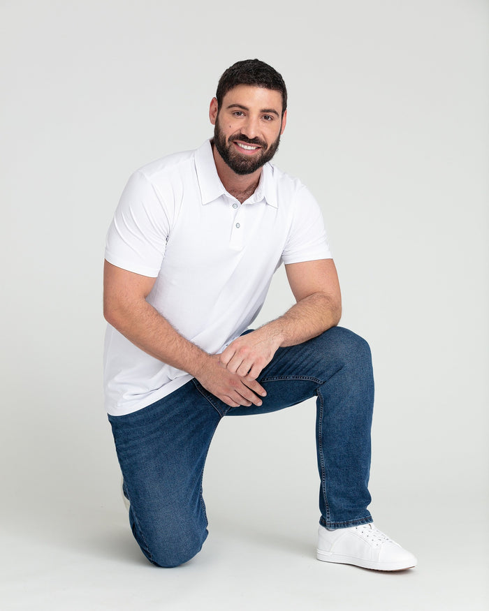 Man wearing white short-sleeve polo shirt and medium blue slim fit jeans with white sneakers.