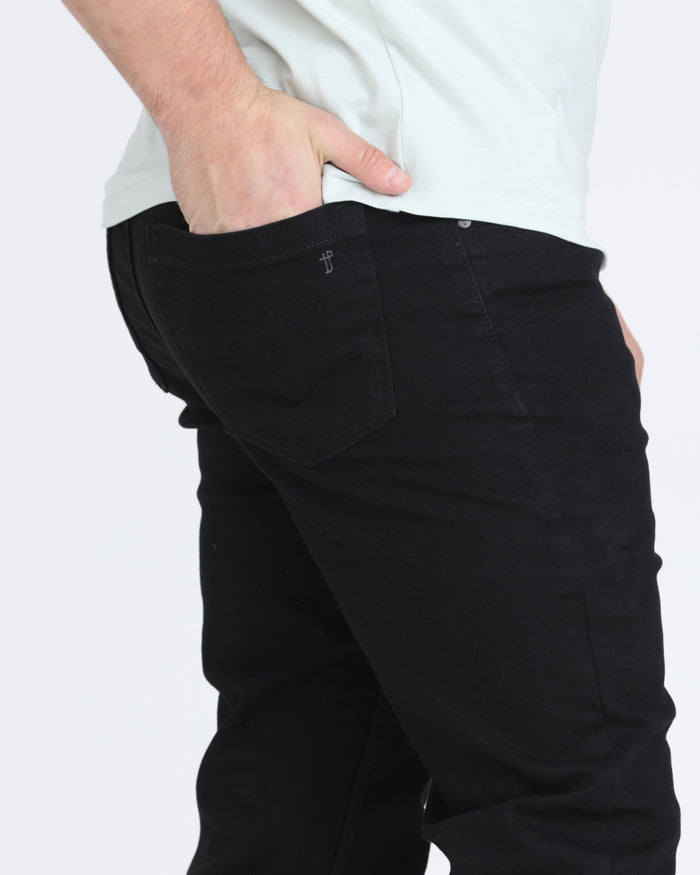 Man wearing black slim fit jeans with white shirt, showing waistband and rear pocket detail.