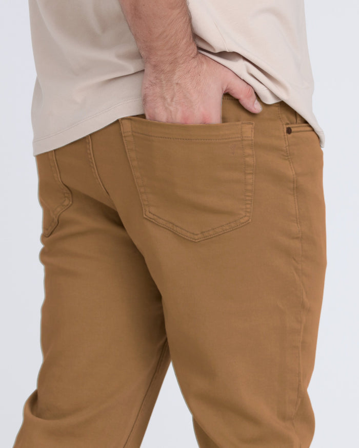 Brown tobacco-colored slim fit pants with back pocket detail worn with cream button-up shirt.