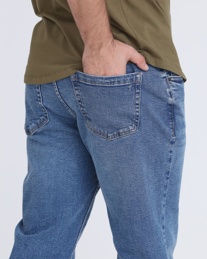 Medium blue ripped jeans with pocket detail on model wearing olive shirt.