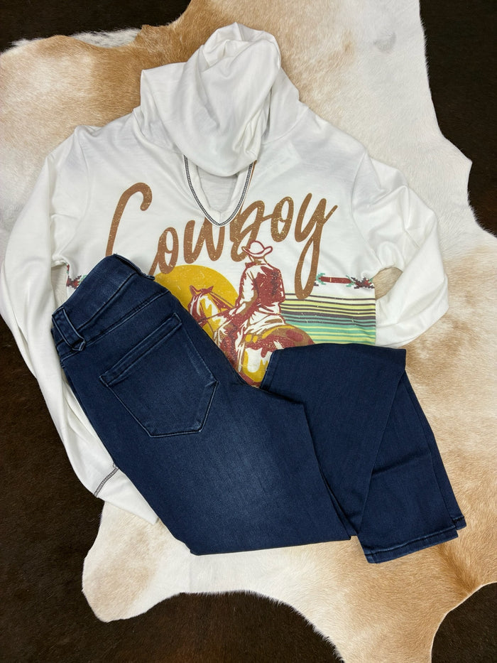 White hoodie with 'Cowboy' graphic and blue jeans on a cowhide rug