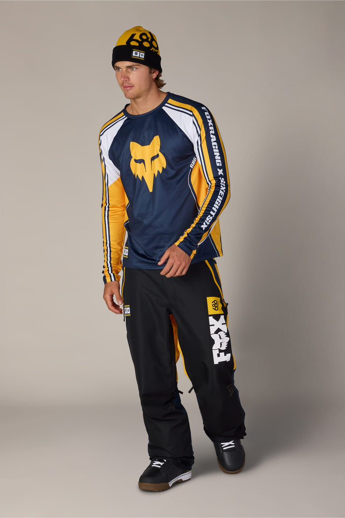 A man wearing a 686 Men’s Fox Racing Base Layer LS, matching snow pants, and a beanie.
