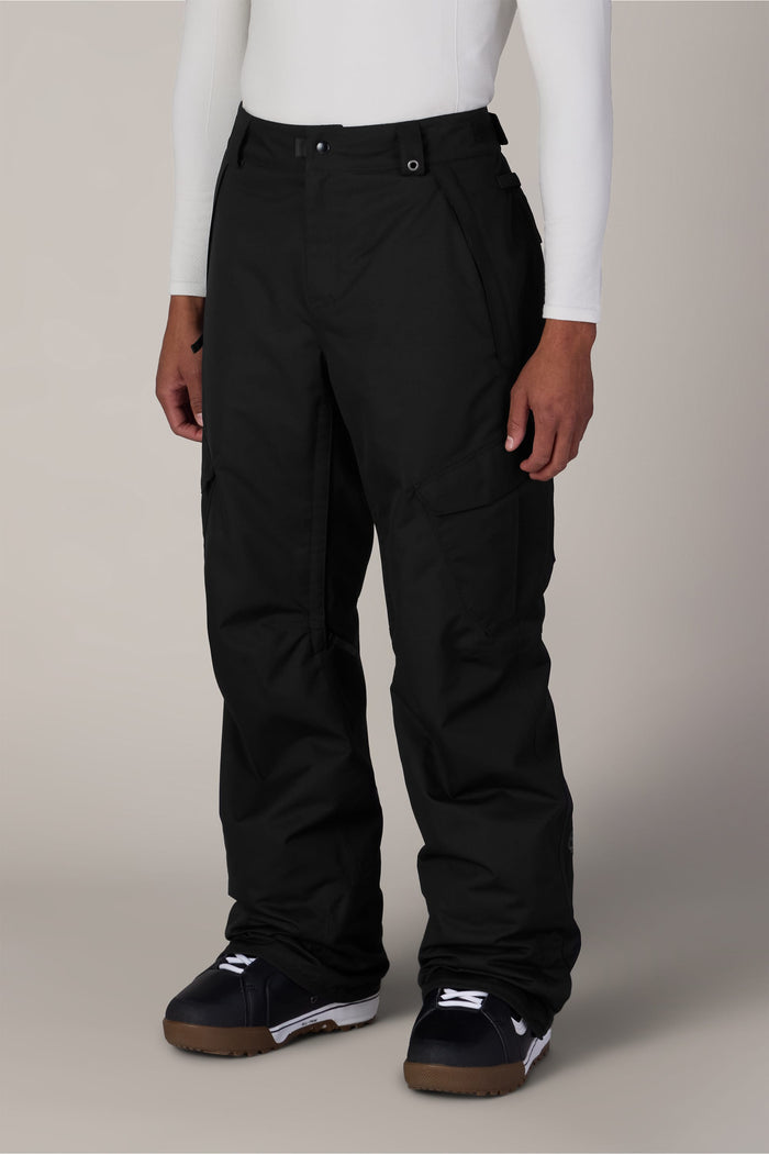 A person wearing a white long-sleeve shirt, the 686 Men’s Infinity™ Insulated Cargo Pant in black, and black snowboard boots stands against a plain background.