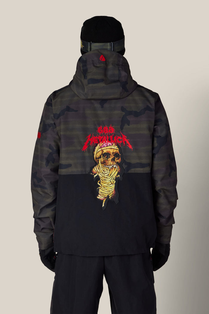 Back view of a person wearing a dark camouflage and black 686 Men’s Metallica One Insulated Jacket, featuring a Metallica mummy skull graphic on the back.