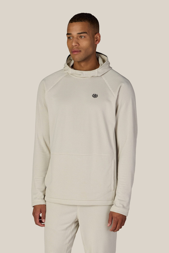 A man wearing the 686 Men’s Mission Grid™ Raglan Hoody in light beige stands facing slightly to the side against a plain beige background.
