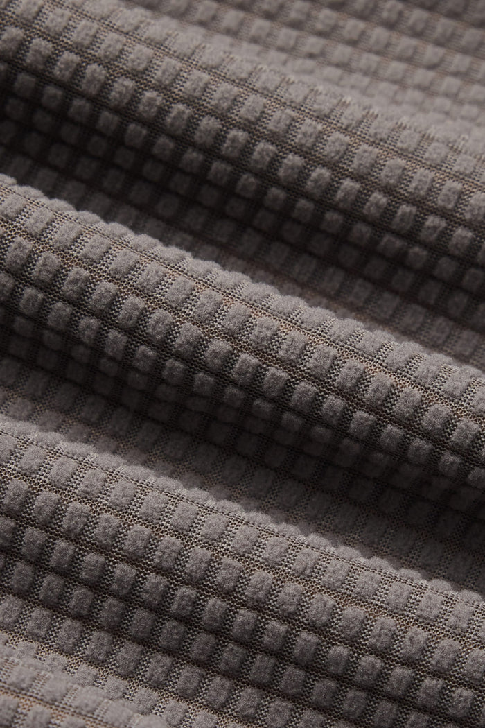 Close-up of gray fabric with a waffle texture, featuring a grid pattern and gentle diagonal folds—characteristic of the cozy 686 Men’s Mission Grid™ Raglan Hoody by 686.