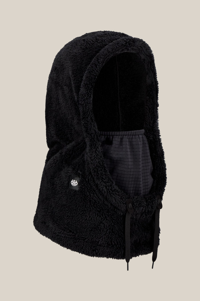 The 686 Tarmac Sherpa Hood by 686 is a black, fuzzy polyester knit hood featuring a face covering and adjustable drawstrings, shown against a plain beige background.