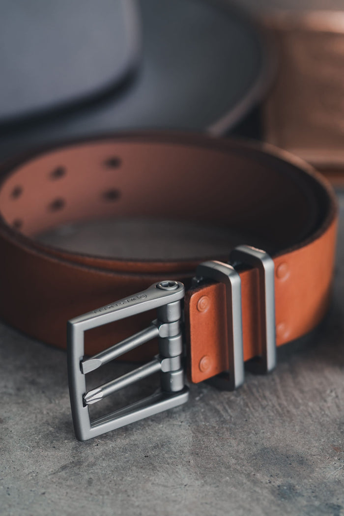 The 686 Westwell Voyager Belt by Westwell is shown up close on a grey surface, featuring brown leather, a silver metal double-prong buckle, metal loops, visible stitching, and multiple adjustment holes.