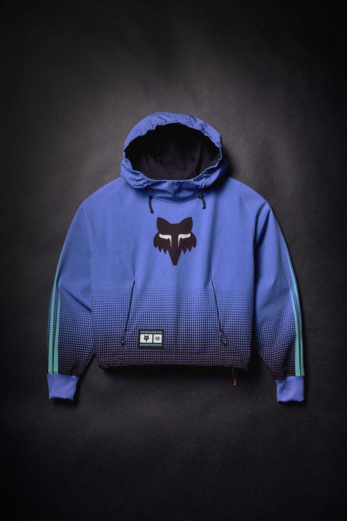 686 Women’s Fox Racing Waterproof Crop Hoody in a blue and black gradient, featuring a Fox head logo on the chest and a brand patch near the hem.