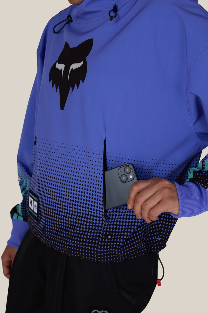 A person wearing a 686 Women’s Fox Racing Waterproof Crop Hoody, placing a smartphone into a zippered chest pocket.