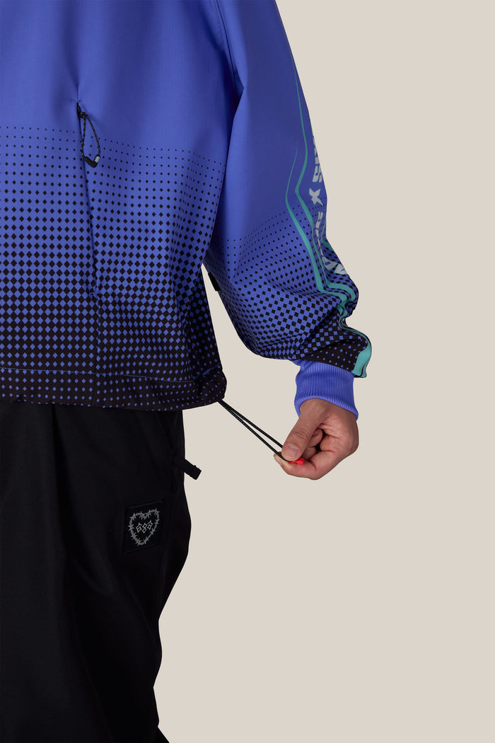 A person wearing a 686 Women’s Fox Racing Waterproof Crop Hoody and black trousers, pulling a drawstring at the jacket’s hem.