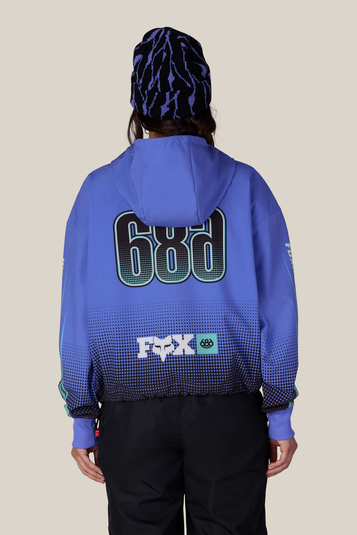 A person from behind wearing a 686 Women’s Fox Racing Waterproof Crop Hoody paired with a patterned blue and black beanie.