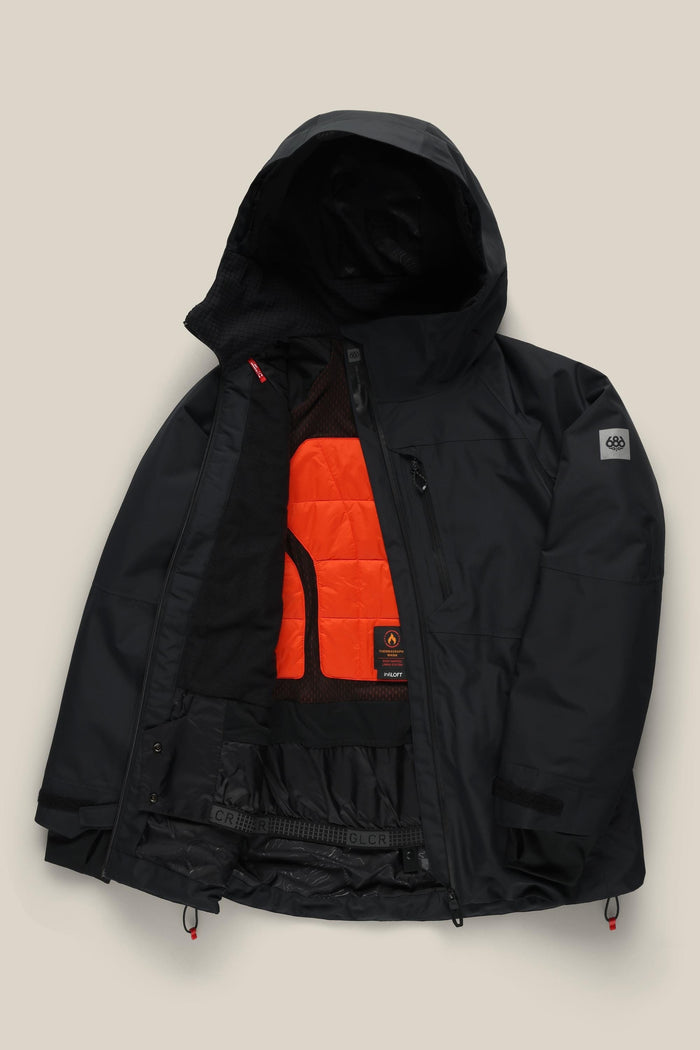 The 686 Women’s Hydra™ Thermagraph® Jacket by 686 is a black hooded winter jacket with a partially open front that reveals an orange quilted inner lining and mesh pockets. It features zippered pockets and a logo patch on the sleeve.