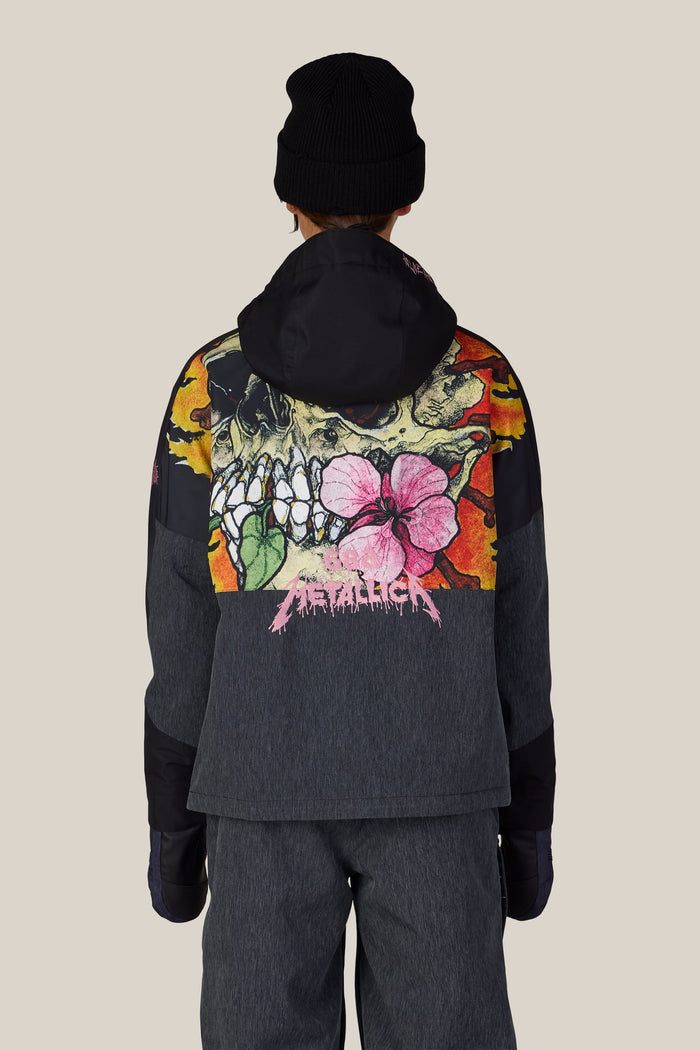 Back view of a person wearing a black beanie and the 686 Women’s Metallica Burning Skull Insulated Jacket, a dark gray waterproof jacket featuring a large graphic of a skull, flames, and a pink flower with the Metallica logo in pink.