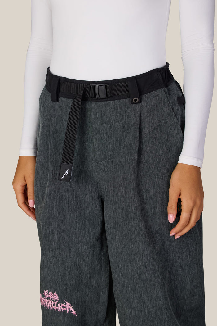 Dark grey waterproof woven 686 Women’s Metallica Burning Skull Shell Pant featuring a black webbing belt and a pink Metallica logo on the lower leg.