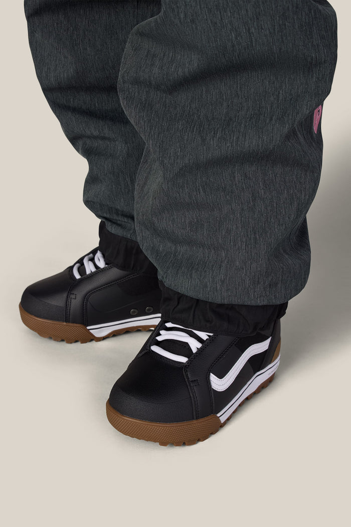 A person wearing charcoal grey 686 Women’s Metallica Burning Skull Shell Pants tucked into black sneakers with white laces and gum-colored soles.