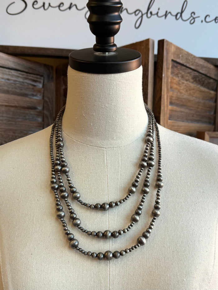 Silver triple-row graduated bead necklace on a mannequin bust, layered dotted pattern