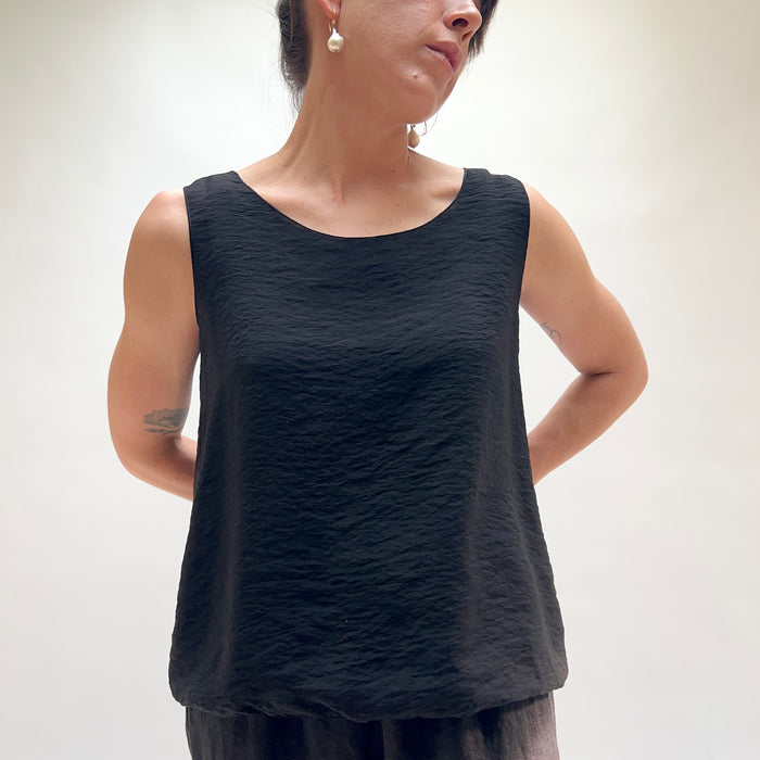 Person wearing a black sleeveless top against a plain background