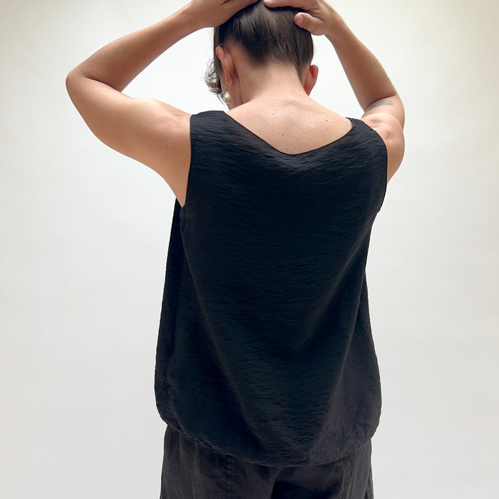 Person wearing a black sleeveless top and dark pants against a white background, viewed from the back