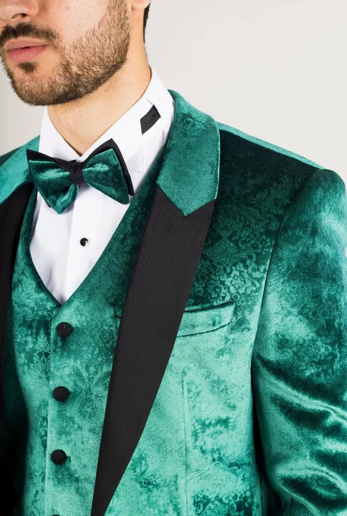 Close-up of a man in a green velvet tuxedo with detailed fabric pattern, black buttons, and matching bow tie, stylish formal wear