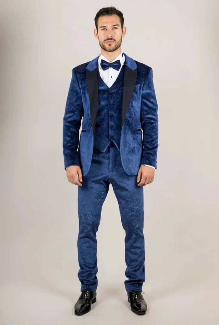 Front view of a man in a blue velvet tuxedo with a matching vest, white shirt, and bow tie, posing with a neutral expression.