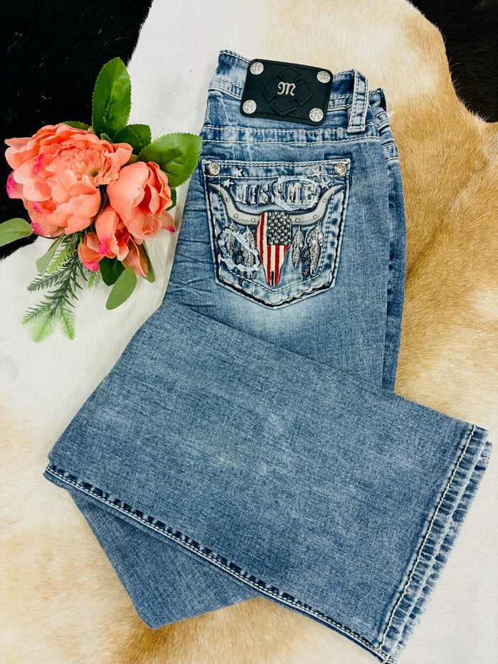 Folded blue jeans with an American flag design on a textured surface with flowers.