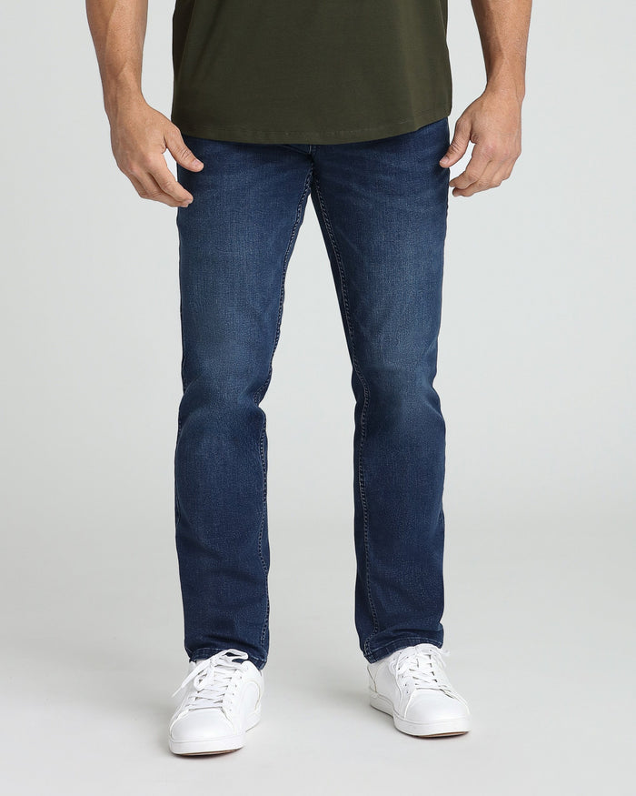 Man wearing medium blue athletic fit jeans with olive green t-shirt and white sneakers.